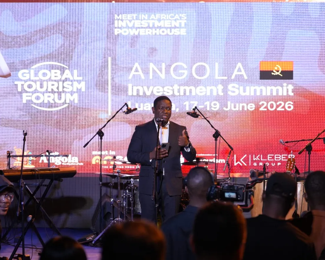 A speaker on stage at the Angola Investment Summit, with a large screen behind reading Angola Investment Summit
