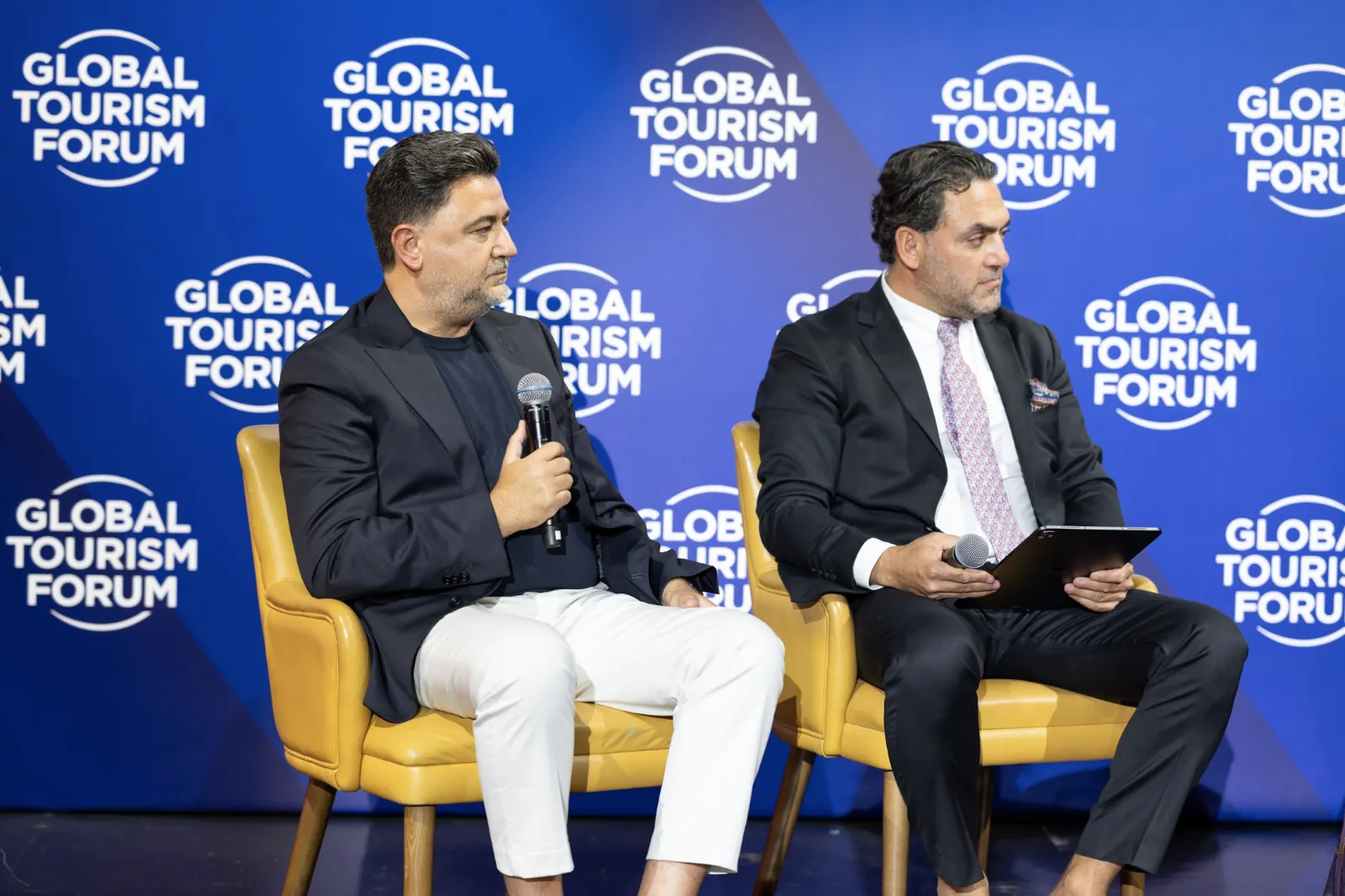 Two speakers seated in yellow chairs on a Global Tourism Forum panel stage