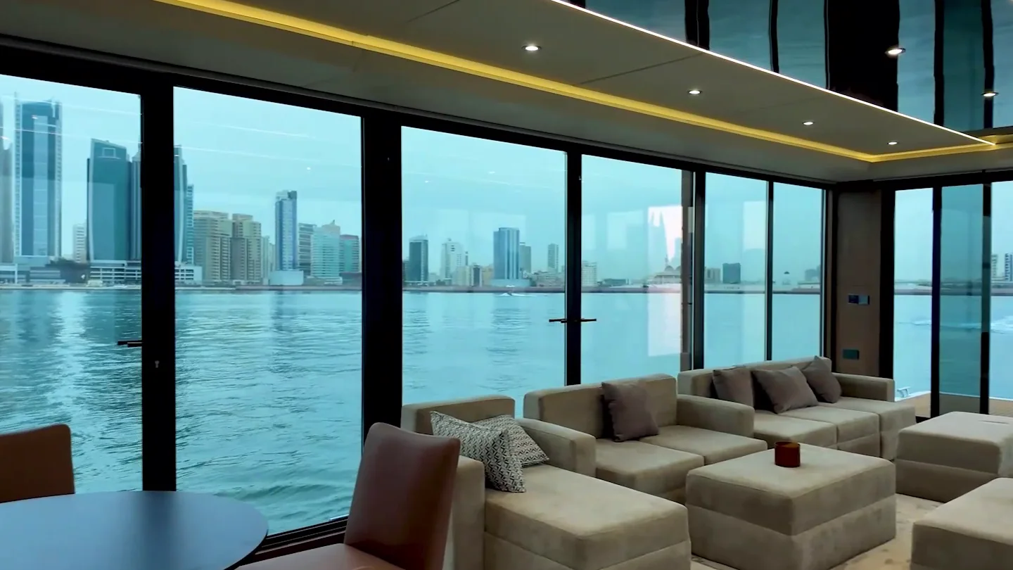 Majlis lounge with low cream sofas behind full-height glass looking onto the water