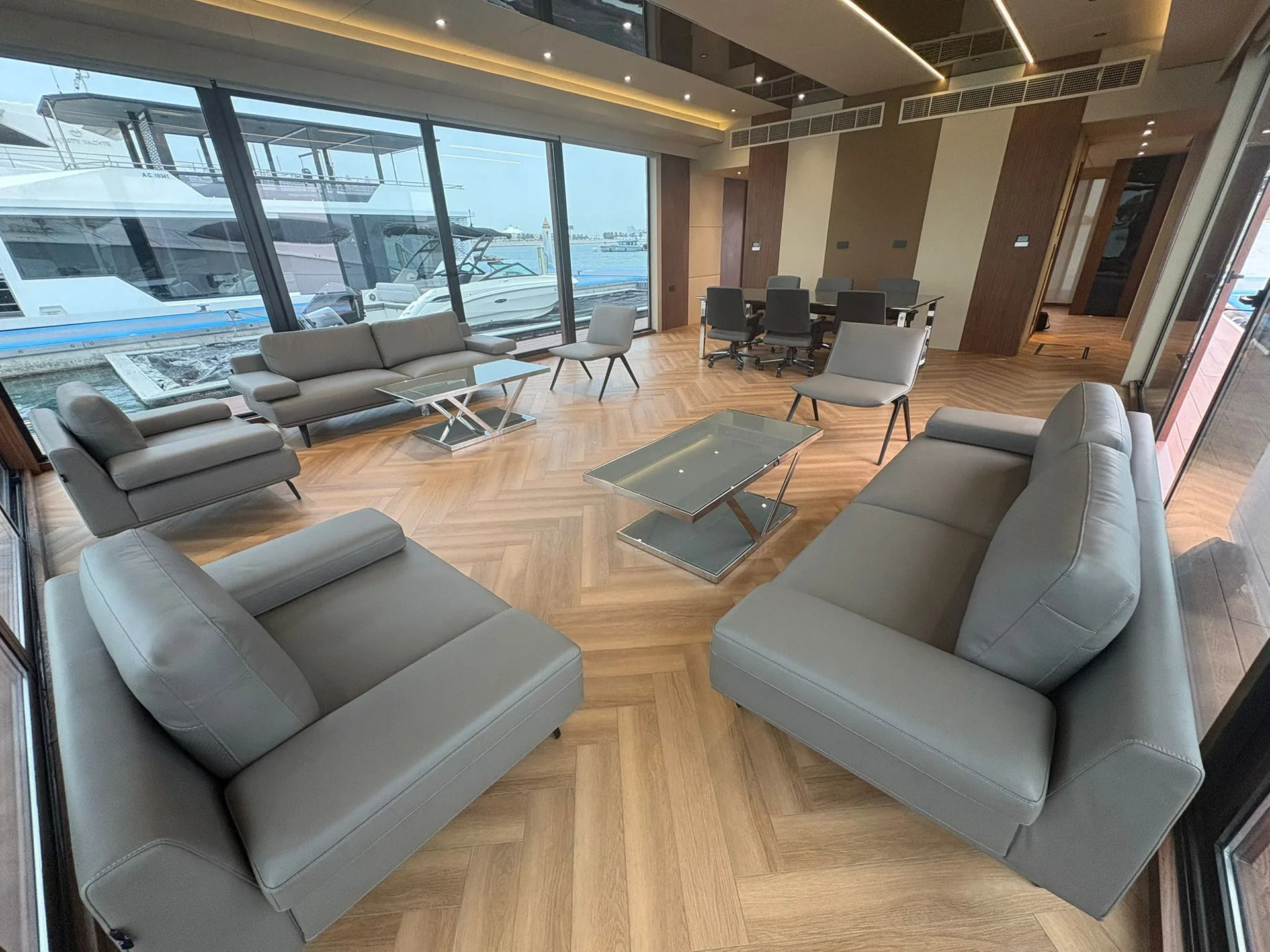 Lounge with grey sofas and armchairs on a herringbone timber floor, glass walls all round