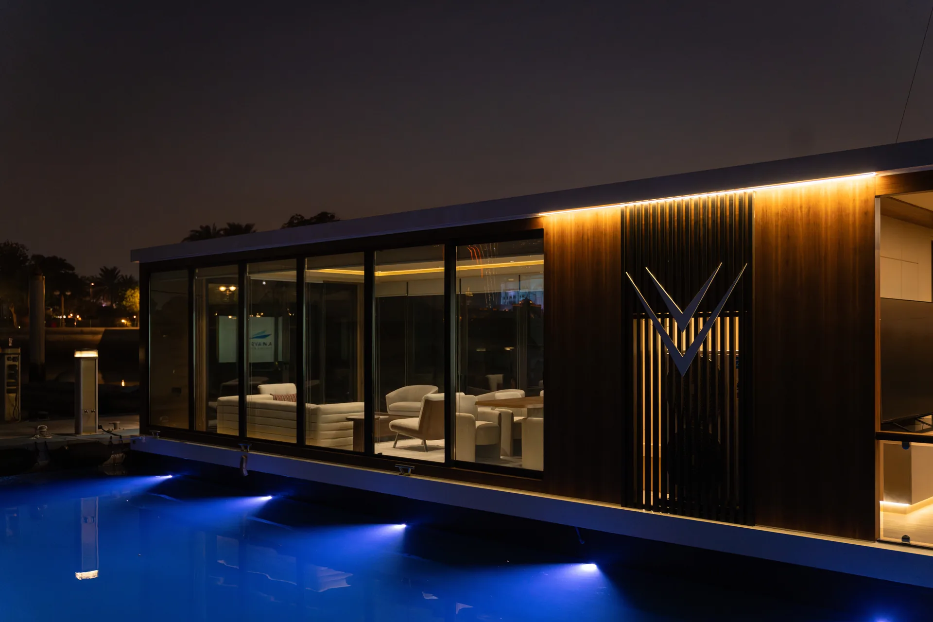 The floating office at night, its interior lit and blue lights along the waterline
