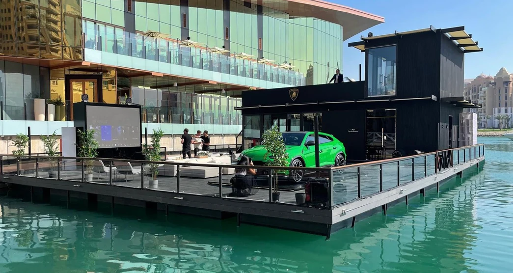 سيارة Lamborghini خضراء على السطح المفتوح لصالة عرض عائمة في اللؤلؤة بالدوحة، وخلفها جناحها الأسود